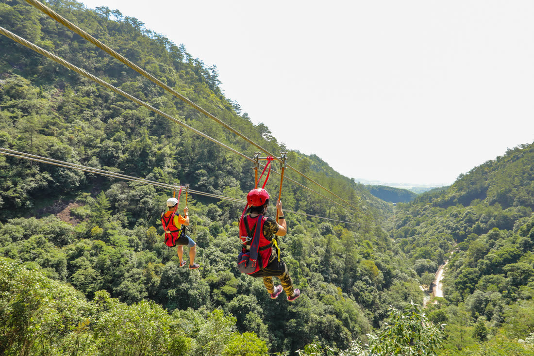Two riders descending a zipline over a river valley
